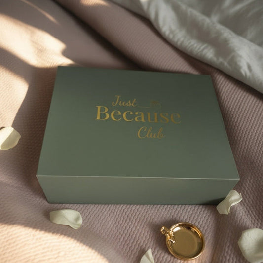 Green box with 'Just Because Click' text on a pink surface with gold ring and petals.