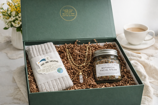 Open luxury green gift box filled with self care items including cosy socks, gold necklace and botanical facial steam.